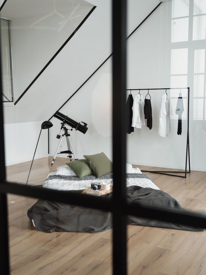 Cozy attic bedroom with telescope, clothing rack, and futon in minimalist style