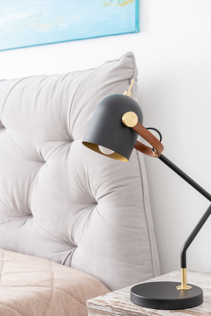 Stylish black lamp on nightstand at modern cozy bed with gray soft headboard in light bedroom